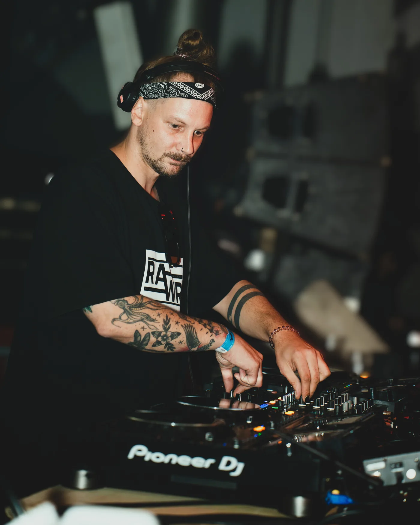 DAY SHO mixing on Pioneer CDJs, headphones on, tattooed arms over the decks
